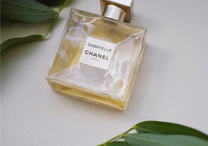 A bottle of gabrielle chanel perfume surrounded by green leaves