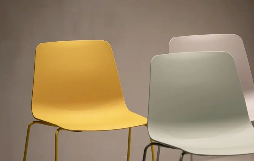 There are three colorful chairs in a bright room.